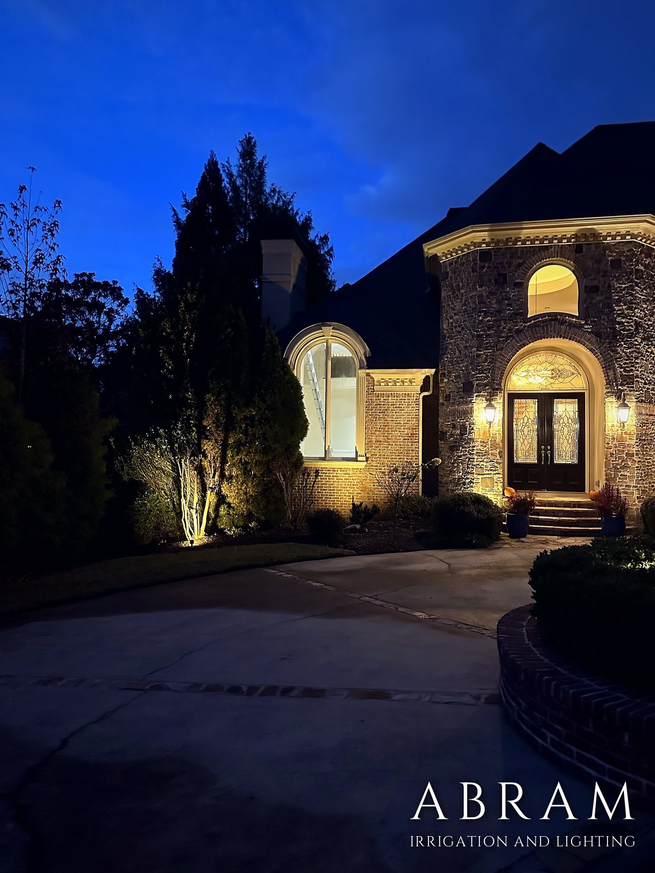 Stone home facade washed with warm uplighting at blue hour